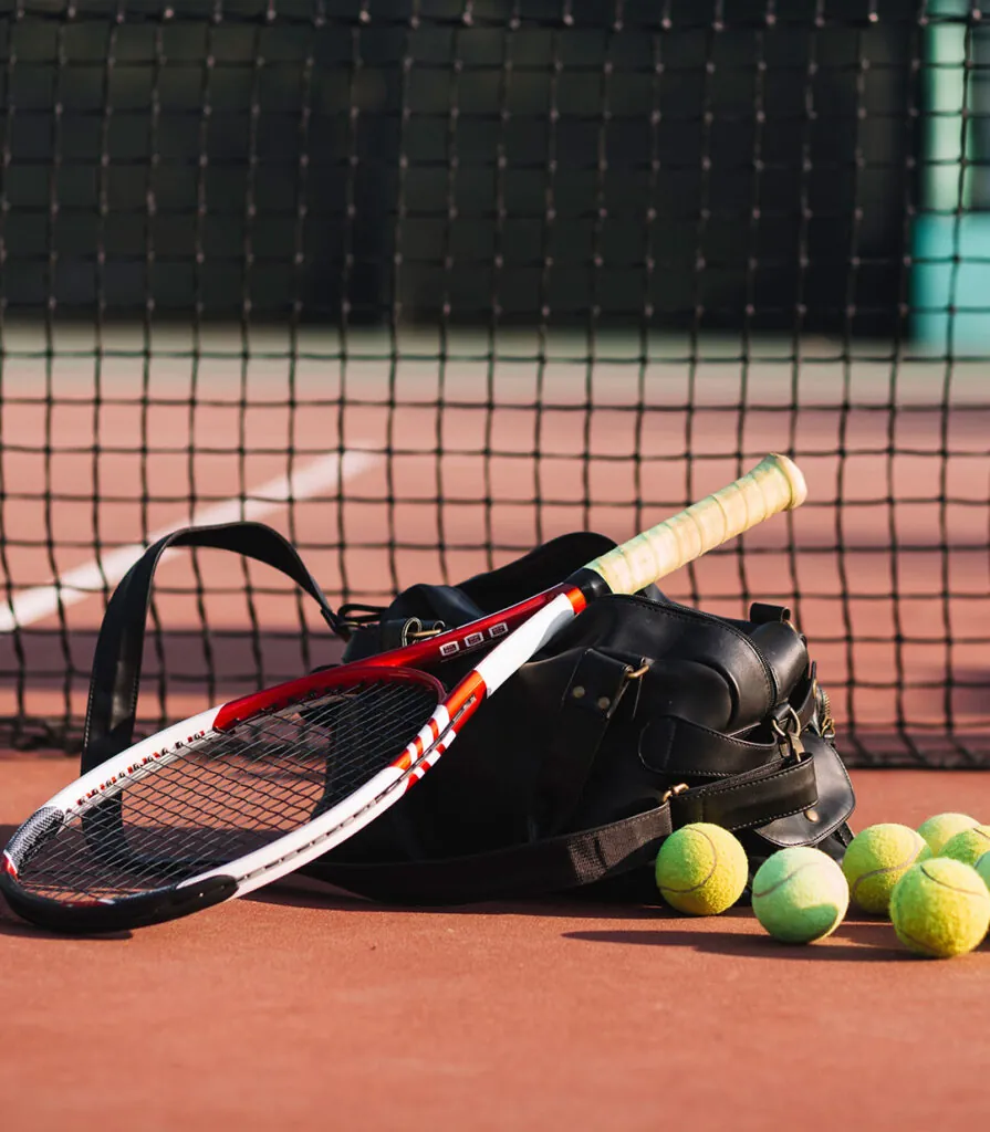 A racquet, kit bag and loose balls at the foot of the net