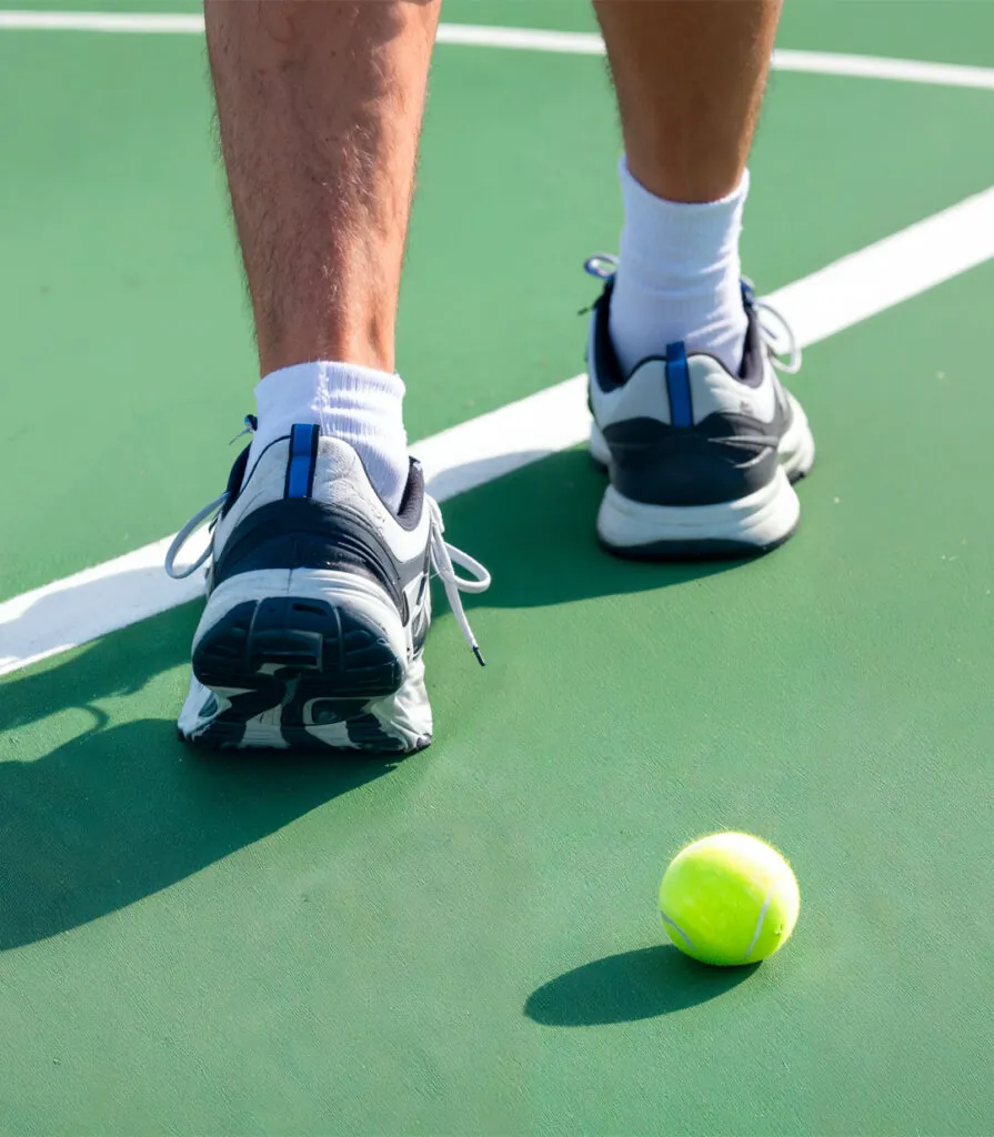 A player’s feet set on the baseline beside a ball at rest