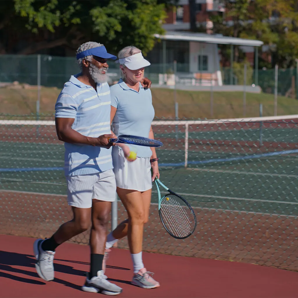 Two older players walking the court together, racquets and ball in hand