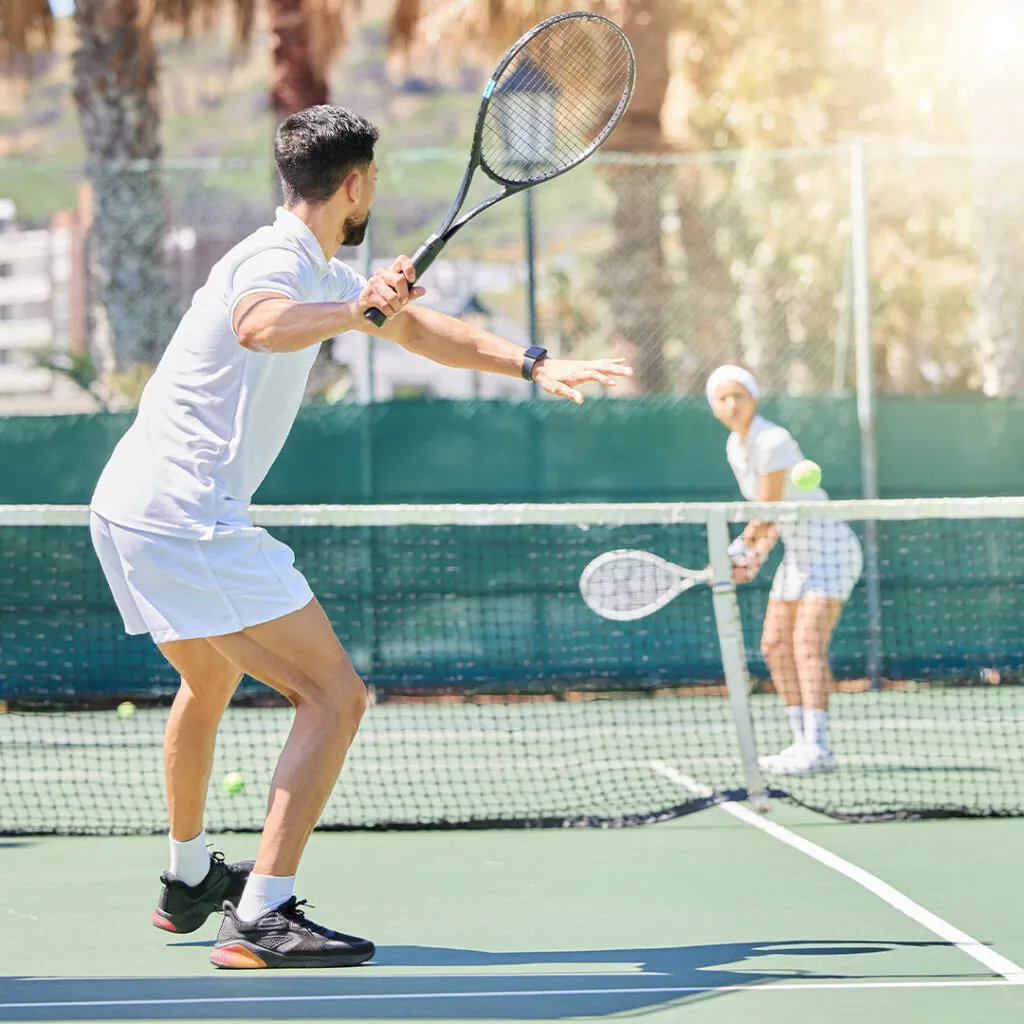 Two players rallying across the net in a sunlit singles drill