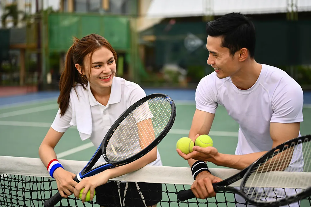 Two coaches talking across the net, racquets and balls in hand
