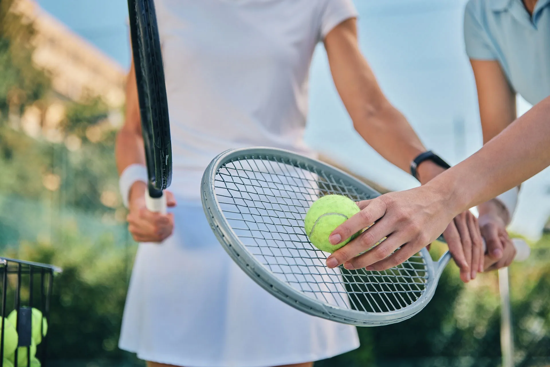 A coach steadying a ball on the strings of a player’s racquet at the net