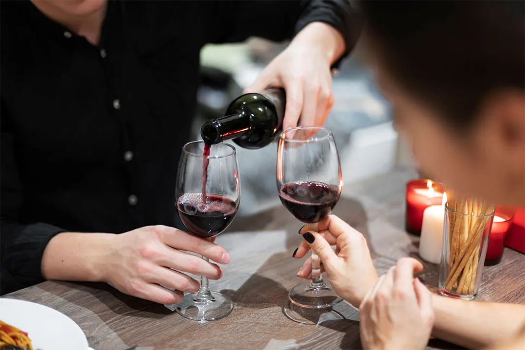 烛光餐桌旁，一人正为两只酒杯斟上红酒