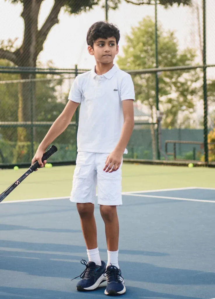 A junior standing at the baseline with his racquet at his side