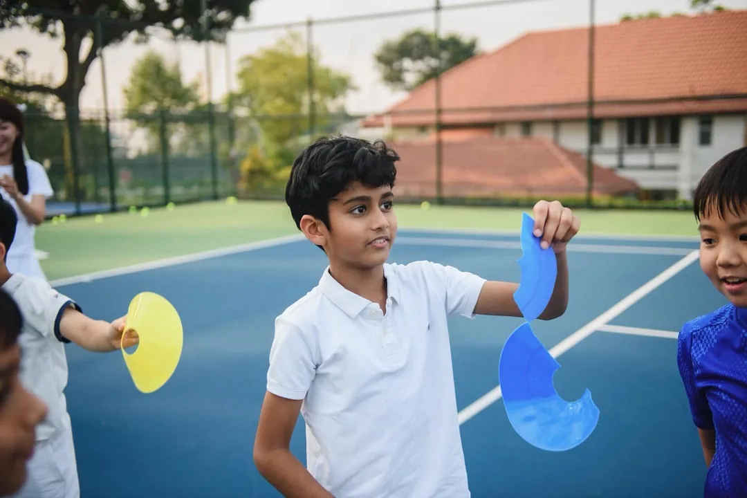 A boy holding up a yellow and a blue marker disc