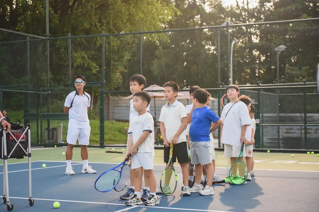 Juniors with racquets gathered beside the ball cart