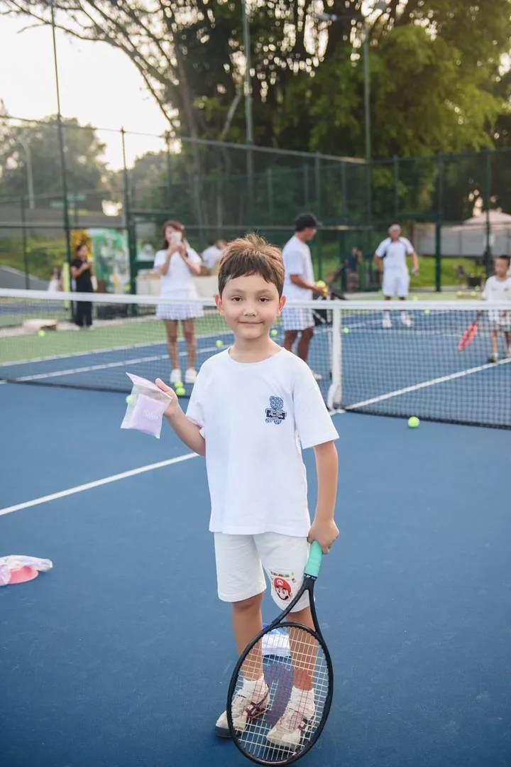 A boy on court holding his racquet and a goodie bag